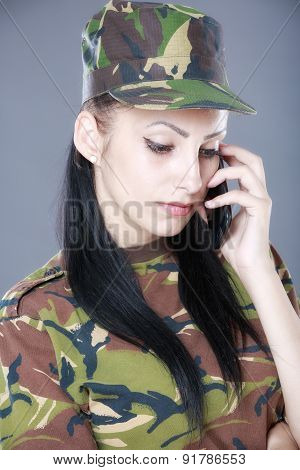 Image of attractive female soldier talking on cell phone against gray background