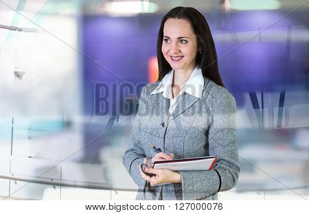 Attractive woman in suit with note pad in the office against of glass reflection. Business background.