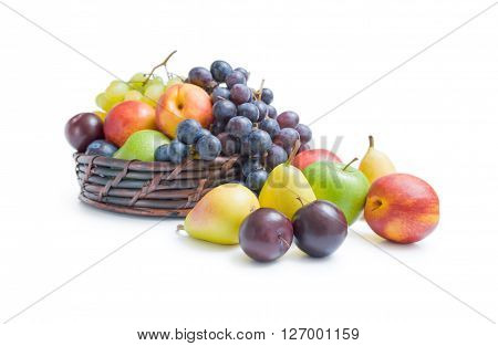 Mix of various fresh ripe fruits plums apples pears peaches and grapes placed in a wicker basket and around isolated on a white background.