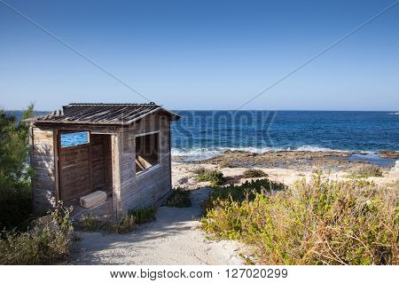 A service old wood house on a sunny beach with rocks and waves