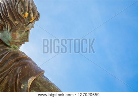 A bronze ancient weathered statue over a blue sky