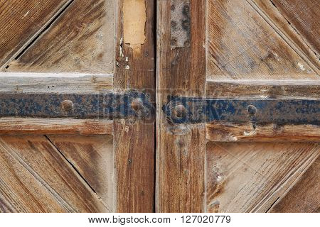 Portion of a weathered wood brown door with his hinges