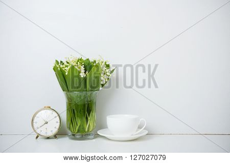 Simple home decoration, lilies of the valley in a vase on the shelf by the white wall background