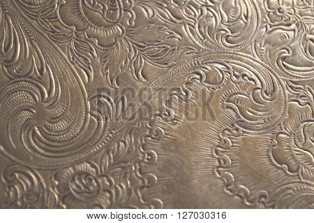 Closeup of tarnished antique silver with scrollwork carving and flowers.