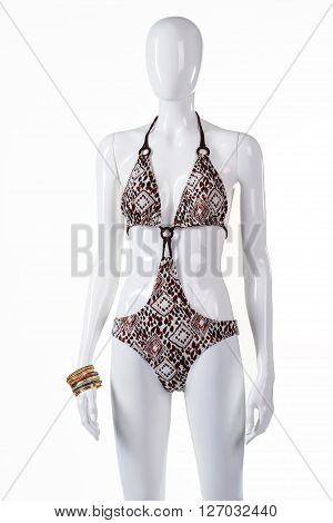 Single piece swimsuit with ornament. Mannequin wearing swimsuit and bracelets. Lady's swimwear and accessories. Lycra swimsuit on display.