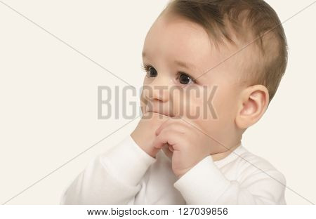 Adorable baby portrait with the hand in the mouth. Cute baby boy looking to the side curious. Isolated on white.