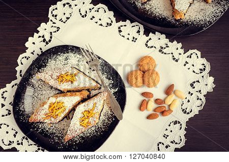 Torta di riso. Baked rice pudding dessert sweetened with sugar powder and garnished with candied orange peels in the top with a fork on the side. Rice cake with almonds and amaretto. Top view.