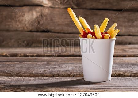Fries with sauce in cup. French fries with tomato ketchup. Aged table with tasty snack. Popular fast food dish.