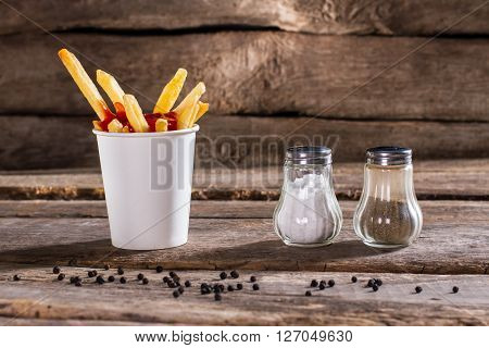 Cup of fries with pepperbox. Salt, pepperbox and fries. Fast food snack on table. So fresh and crispy.