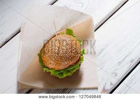 Big burger on a stick. Burger laying on paper wrap. Beefburger for breakfast. Well-made dish in bistro.