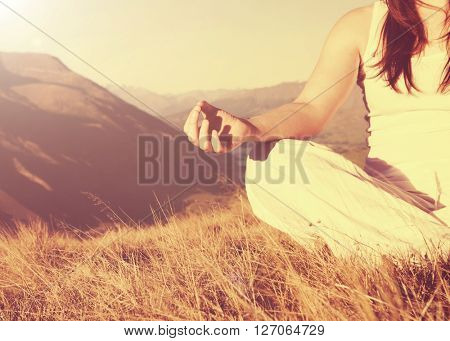 Lady meditating in lotus position on top of the mountain.
