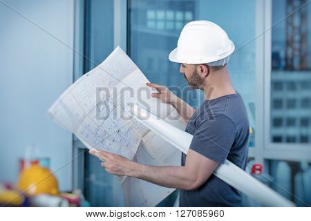 Portrait of an architect builder studying layout plan of the rooms, serious civil engineer working with documents on construction site, building and home renovation, professional foreman at work