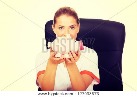 Smile doctor sitting behind the desk and holding a piggybank