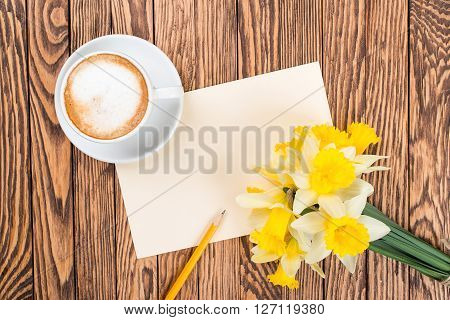 A cup of coffee next to the spring white flowers on wooden texture. Space for text.