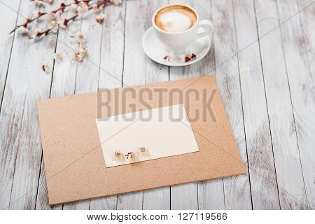A cup of coffee next to the spring white flowers on a wooden texture. Space for text.