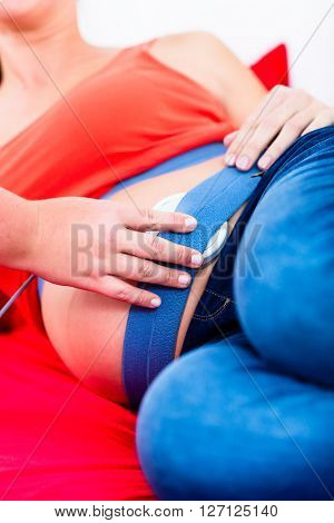Belly of pregnant women on couch with CTG scanning being adjusted 