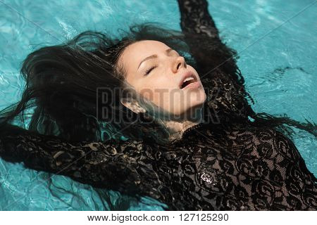 Portrait of the beautiful woman in black dress floating in blue water