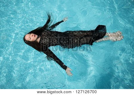 Beautiful woman in black dress floating in blue water