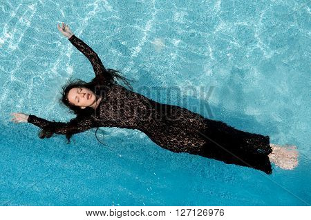 Beautiful woman in black dress floating in blue water