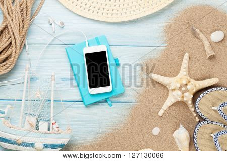 Smartphone and notepad on wooden table with starfish and shells. Top view with copy space