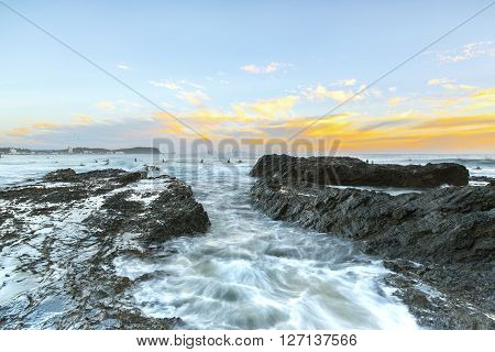 Surfers at Currumbin Rock Gold Coast at sunset, with ocean current rushing through the rock.