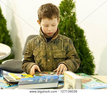 KYIV UKRAINE - APRIL 21, 2016: Unidentified boy carefully reads books at children showcase of the 6th Festival BOOK ARSENAL on April 21, 2016. Guests of the fair were Lars Svendsen Vigdis Hjorth Etgar Keret