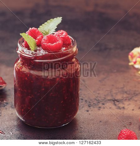 Raspberry jam with mint, close up. A jar of raspberry jam and fresh raspberries on top.  Macro, selective focus, vintage toned image, blank space