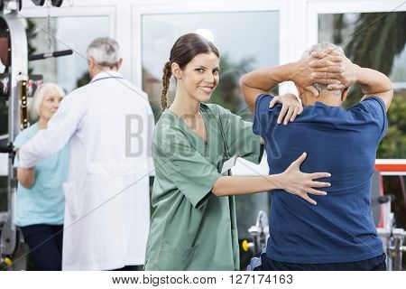 Female Nurse Assisting Senior Man In Back Exercise