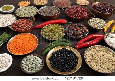 Beans peas and lentils in metal bowls on dark background.