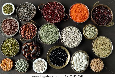 Beans peas and lentils in metal bowls on dark background.