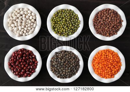 Colorful beans and lentils in ceramic bowls on a dark background.