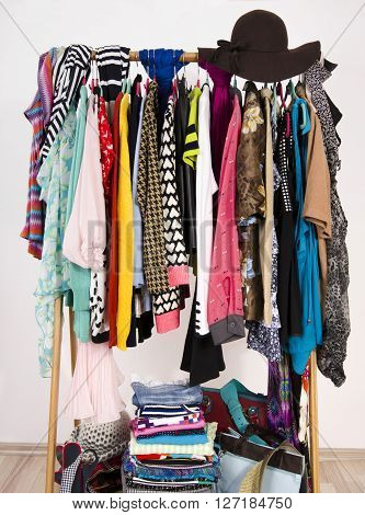 Many colorful clothes on hangers in a store. A lot of clothes and accessories hanging on a rack nicely arranged on hangers and in piles.