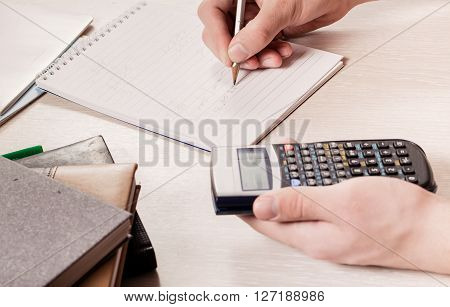 The hands of the person holding the calculator and a pencil. Calculation of people writes down results in a notebook. Close up