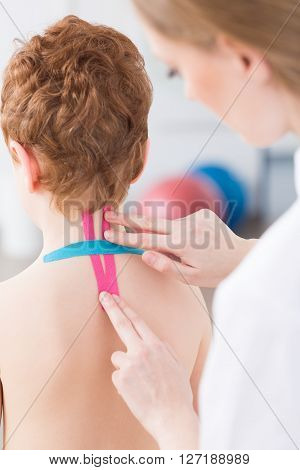 Female physiotherapist applying colorful tapes on little boy's cervical spine
