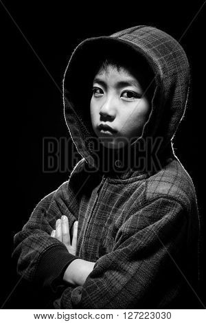 Asian boy in hoodie jacket staring at camera. Black and white shot in studio with back lighting for highlights.
