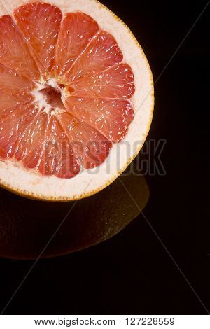 Cut half of juicy ripe grapefruit is reflected in a black surface