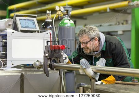 Industrial operator setting  computer controlled process of orbital welding machine in  stainless steel pipes manufacturing workshop.