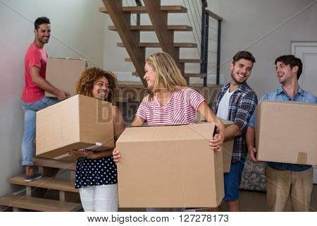 Cheeerful friends carrying cardboard boxes while relcocating in new house