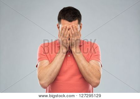 people, crisis, emotions and stress concept - man in t-shirt covering his face with hands over gray background