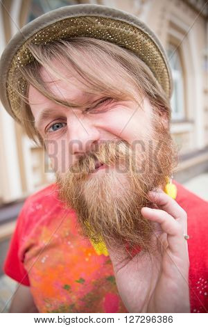 Hipster bearded man combing his beard outdoors. Blond man in straw hat looking so funny with such a reaction to the sun.