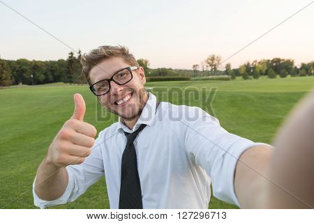 Handsome smiling man making selfies and showing thumb-up isolated on green environment. Man in glasses smiling for the camera.