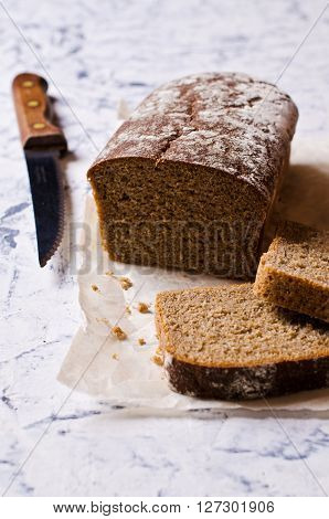 Cut loaf of rye bread on paper. Concrete background. Selective focus.