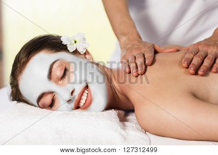 Young beautiful woman with cly mask lying on massage table and enjoying massage. Spa concept,