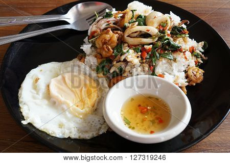 Rice topped with spicy fried squid basil leaves and fried egg (Thai food)