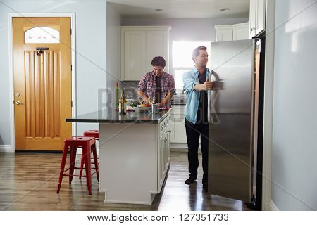 Male couple in the kitchen preparing a meal, opening fridge