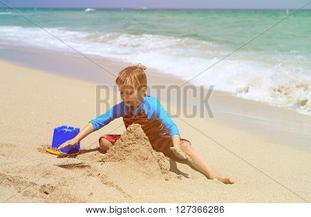 cute little boy play with sand on summer beach