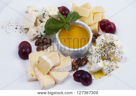 cuts of a variety of cheeses with grapes and nuts on a white plate