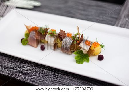 Salted and marinated herring on creamy cheese, beer and black bread chips, potatoes and red caviar