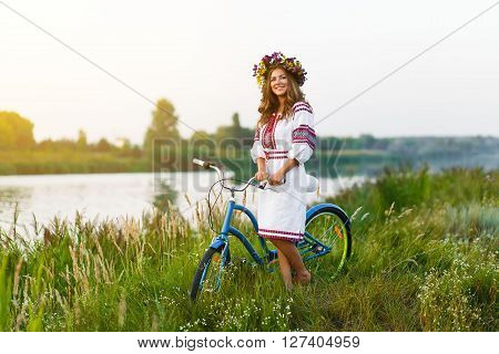 Woman in Folk costume with bicycle. Young attractive woman at the riverside having rest with bicycle in national ethnic ukrainian folk traditional costume or dress.
