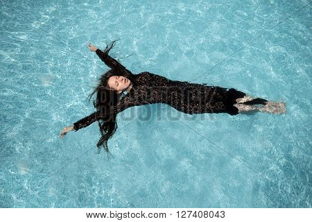 Beautiful woman in black dress floating in blue water